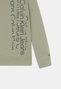 Felpa verde con finitura testurizzata, con grande scritta nera "Calvin Klein Jeans" sul davanti e piccolo logo sulla manica.