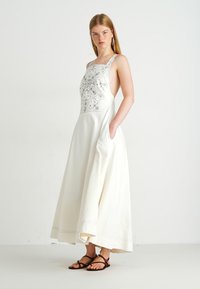 Witte maxidress met een gedetailleerd geborduurd bovenstuk, zijzakken en brede schouderbanden. Heeft een vloeiende silhouet en een nette zoom.