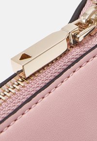 Lyserød kunstlæder clutch med en guldlås, der har en tekstureret stofkant og kontrasterende sort syning langs kanterne.