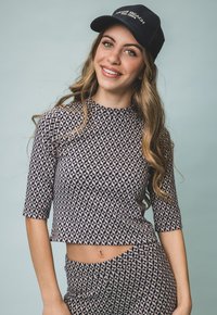 Marineblauw en beige top met geometrisch patroon, drie kwart mouwen en een ronde hals, gecombineerd met een bijpassende onderkant. Zwarte baseballpet.