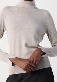 Jasnoszary sweter z golfem wykonany z miękkiej dzianiny, posiada długie rękawy z otworami na kciuki oraz dopasowaną sylwetkę, z detalicznym przeszyciem na szwach.
