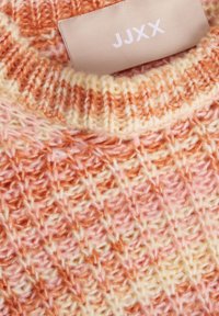 Pletený svetr s měkkou texturou v odstínech broskve, oranžové a krémové barvy. Viditelná etiketa s označením "JJXX".