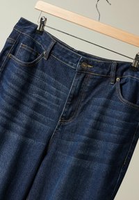 Tummansiniset farkut klassisella leikkauksella, viiden taskun suunnittelulla ja kontrastitikkauksella. Varustettu nappisuljennalla ja roikkuklipillä.