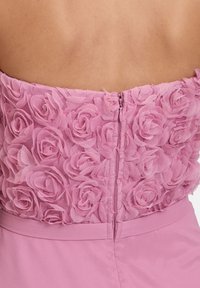 Robe rose avec un design floral texturé composé de roses en tissu superposées sur le corsage, dotée d'une fermeture éclair au dos.