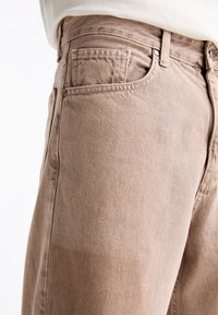 Jeans de talle alto en beige, confeccionados en denim suave. Incluyen un bolsillo delantero, pasadores para cinturón y una textura sutil con un acabado suave.