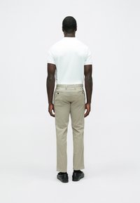 Herrenausstattung mit einem weißen Kurzarmhemd und beigen Hosen aus glattem Stoff, dazu schwarze Schuhe und dezente Nähte.