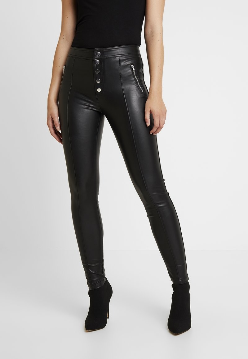 Pantalon taille haute en cuir synthétique noir avec braguette à boutons et poches latérales zippées, présentant une coupe slim et une texture lisse.