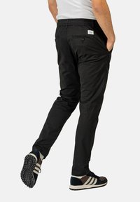 Schwarze Cargo-Hosen mit elastischem Bund, Seitentaschen und einer lockeren Passform. Hergestellt aus einem strapazierfähigen Stoff mit sichtbaren Nähdetails.