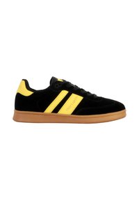 Zapatilla de ante negra con acentos amarillos y tres rayas, que cuenta con una suela de goma y cordones negros. Diseño limpio y minimalista.