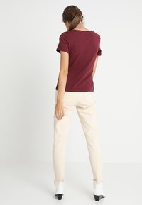 Camiseta corta de manga en color burdeos con cuello redondo, combinada con pantalones ajustados color crema y botas negras de tobillo con acabado brillante.