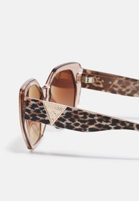Ochelari de soare cu imprimeu de leopard maro, cu un cadru transparent de culoare roz și un accent triungiular cu logo auriu pe brate.