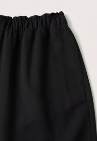 Tissu noir élastique à la taille, texture lisse avec couture latérale visible et détail de poche sur fond clair.