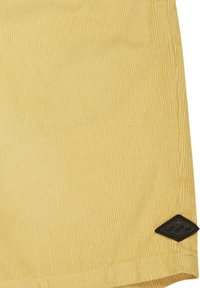 Pantalones cortos de pana amarillos con una superficie texturizada, que presentan un parche con un logo de diamante negro en la esquina inferior derecha.