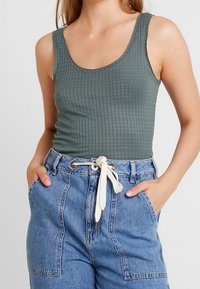 Top verde a costine con scollo a girocollo, abbinato a pantaloni corti in denim azzurro chiaro con vita regolabile e tasche.