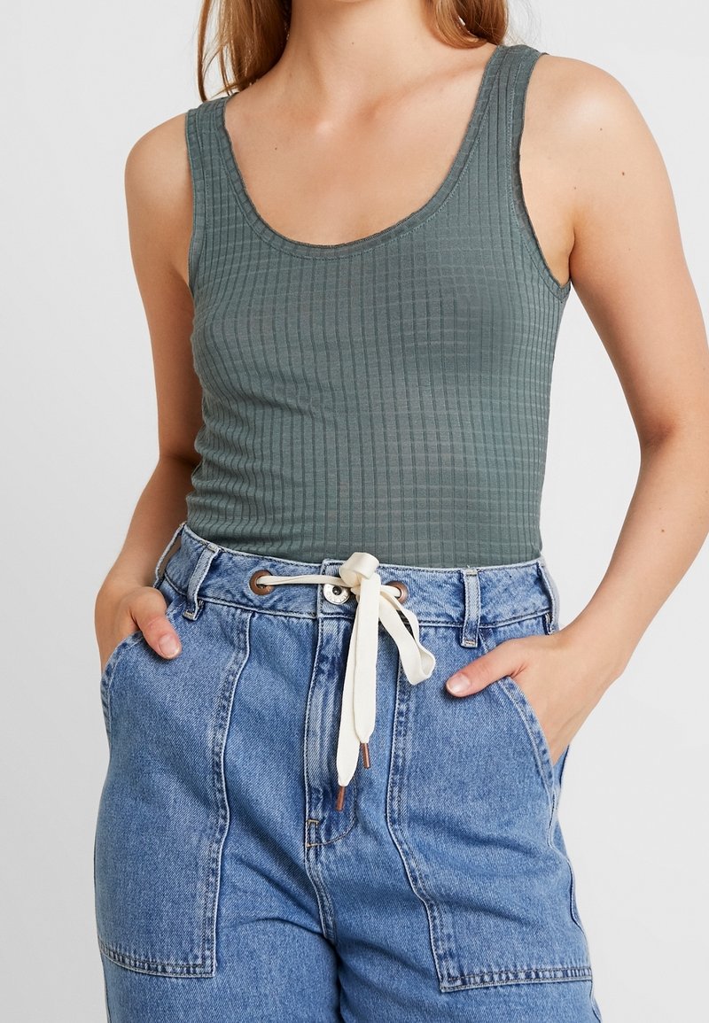 Top verde a costine con scollo a girocollo, abbinato a pantaloni corti in denim azzurro chiaro con vita regolabile e tasche.