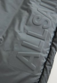 Svart vadderad jacka med en slät, glänsande yta, med upphöjd branding på tyget. Designen har en elegant, minimalistisk stil.