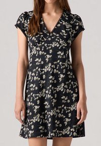 Robe noire avec un motif floral de marguerites blanches, manches courtes et encolure en V. Fabriquée en tissu léger, offrant une coupe décontractée.