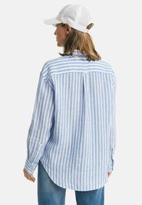 Camicia a righe blu chiaro e bianca con bottoni, maniche lunghe e orlo curvo, abbinata a un cappellino bianco. Tessuto di lino, vestibilità rilassata.