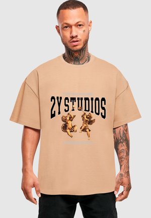 Beiges, übergroßes T-Shirt mit schwarzem, fettem Text und Cherubinen-Designs in der Mitte. Kurze Ärmel mit lockerer Passform. Klare Linien und weiche Textur.