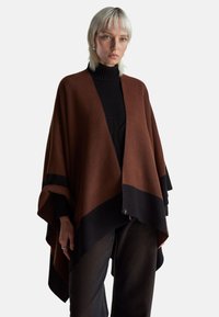 Hnědý a černý pončo z měkké látky, s asymetrickým designem, širokými rukávy a trojúhelníkovým lemem. Vhodné pro vrstvení.