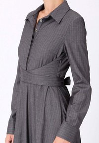 Robe croisée gris à rayures avec manches longues, col pointu et ceinture. Comprend une fermeture à boutons et une texture de tissu lisse.