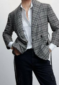 Grijze ruitjes dubbele-breasted blazer met een gestructureerde afwerking, gelaagd over een witte button-up shirt, gecombineerd met donkere broeken.