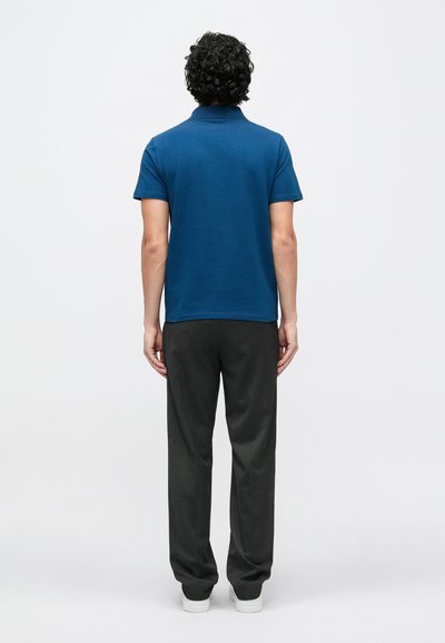 Tumši zils polo krekls ar īsām piedurknēm un apkakli, kopā ar oglekļpelēkām biksēm un baltām sporta kurpēm. Audums izskatās gluds.