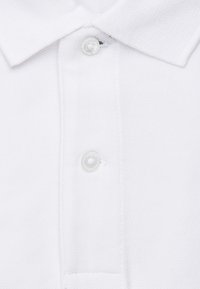 Polo bianco realizzato in un tessuto testurizzato, con colletto corto e due bottoni al collo. Design pulito senza motivi o accenti visibili.