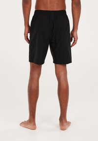 Zwarte zwemshorts met een elastische tailleband en zijzakken, gemaakt van lichtgewicht stof, weergegeven vanaf de achterkant, boven de knie lengte.