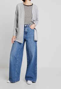 Gray striped cardigan with open front, paired with black and white striped shirt. Wide-leg blue jeans and white sneakers complete the outfit.