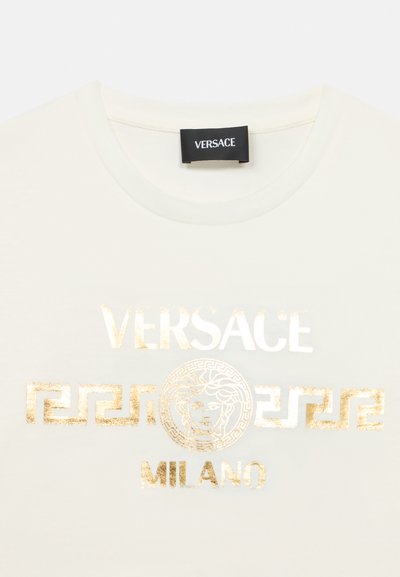 Λευκό μπλουζάκι με χρυσά γράμματα "VERSACE" και "MILANO" με μοτίβο ελληνικού κλει διού και διακοσμητικό λογότυπο Μέδουσας. Στρογγυλή λαιμόκοψη.