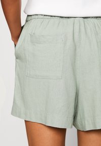 Shorts vert clair en tissu texturé. Ils comportent une ceinture élastique et des poches latérales, avec une coupe décontractée et ample.