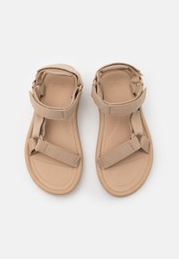 Beige sandals with adjustable fabric straps, a textured footbed, and a flexible, cushioned sole for comfort.
