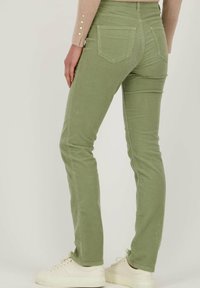 Groene corduroy broek met een slim fit, voorzien van twee achterzakken en een middelhoge taille. Combinatie met crèmekleurige sneakers voor contrast.