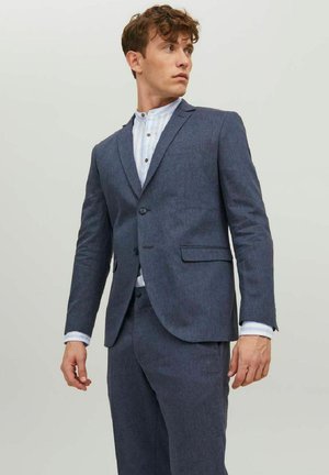 Blazer azul oscuro con hombros estructurados, cierre de un botón y dos bolsillos frontales, combinado con una camisa de rayas clara debajo.