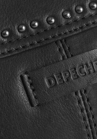 Čierna koža s hladkým povrchom, s radom kovových cvočkov a debossovanou nálepkou s nápisom "DEPECHE." Viditeľné sú prešité švy.