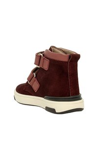 Burgunderfarbene Wildleder-Stiefelette mit zwei Klettverschlüssen, gepolstertem Kragen und weißer Gummisohle. Mit Nähdetails und schwarzen Gummielementen.