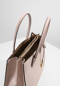 Rosa läderhandväska med texturerad yta, dubbla handtag och dragkedjedetalj i guldfärg. Insidan har brunt foder och dragkedjeficka.