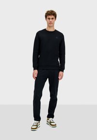 Sudadera negra con cuello redondo, puños acanalados y pantalones oscuros a juego. Las zapatillas casuales tienen cordones blancos y acentos texturizados.