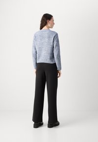 Pull en maille bleu clair, au design court, manches longues. Assorti à un pantalon noir à jambes larges et des chaussures noires épaisses. Texture lisse.
