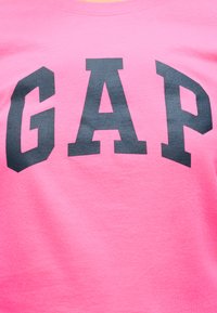 Ροζ ύφασμα με μεγάλα μαύρα γράμματα που σχηματίζουν τη λέξη «GAP» κεντραρισμένα στην επιφάνεια.