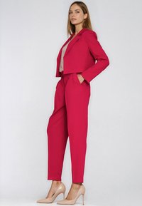 Fuksjowy przycięty blezer i dopasowane spodnie zwężane ku dołowi, wyposażone w kieszenie, o gładkiej fakturze, noszone z cielistymi szpilkami.