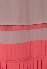 Vestido con una parte superior de color púrpura claro y una banda horizontal, y una falda de coral con pliegues. Textura suave con colores contrastantes.