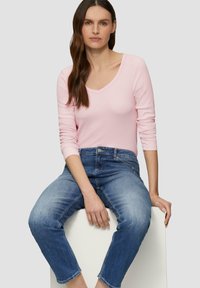 Hellrosa Langarm-V-Ausschnitt-Oberteil, kombiniert mit blauen Denim-Jeans, mit entspanntem Schnitt und dezentem Verblassen des Stoffes.