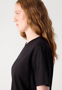 Svart bomull T-skjorte med rund hals og korte ermer. Har et lite brodert detalj på brystet og en jevn tekstur.