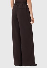Pantaloni a gamba larga realizzati in un tessuto nero e liscio. Presentano una vita elastica, due tasche posteriori e una vestibilità ampia lungo le gambe.