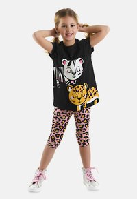 Schwarzes T-Shirt mit Tierdruck, das ein Zebra und einen Leoparden zeigt, kombiniert mit rosa Leggings mit Leopardenmuster. Silberne High-Top Sneakers.