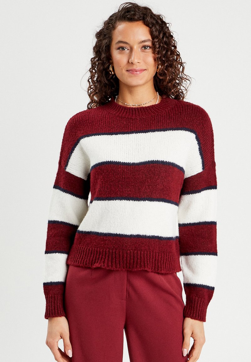 Pull rayé rouge et blanc avec des accents bleu marine, col rond côtelé et poignets, texture douce, ajusté à la taille, coupe ample.