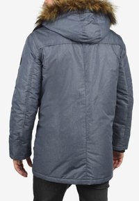 Grå, isoleret parka med en faux fur hætte, der har en tekstureret finish og sidelommer, designet til at holde varme i koldt vejr.