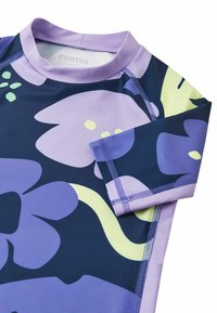Koszulka do pływania z długim rękawem w kolorze granatowym, ozdobiona dużymi fioletowymi kwiatowymi wzorami, podkreślonymi żółto-zielonymi detalami. Gładka tekstura i przeszywane szwy.